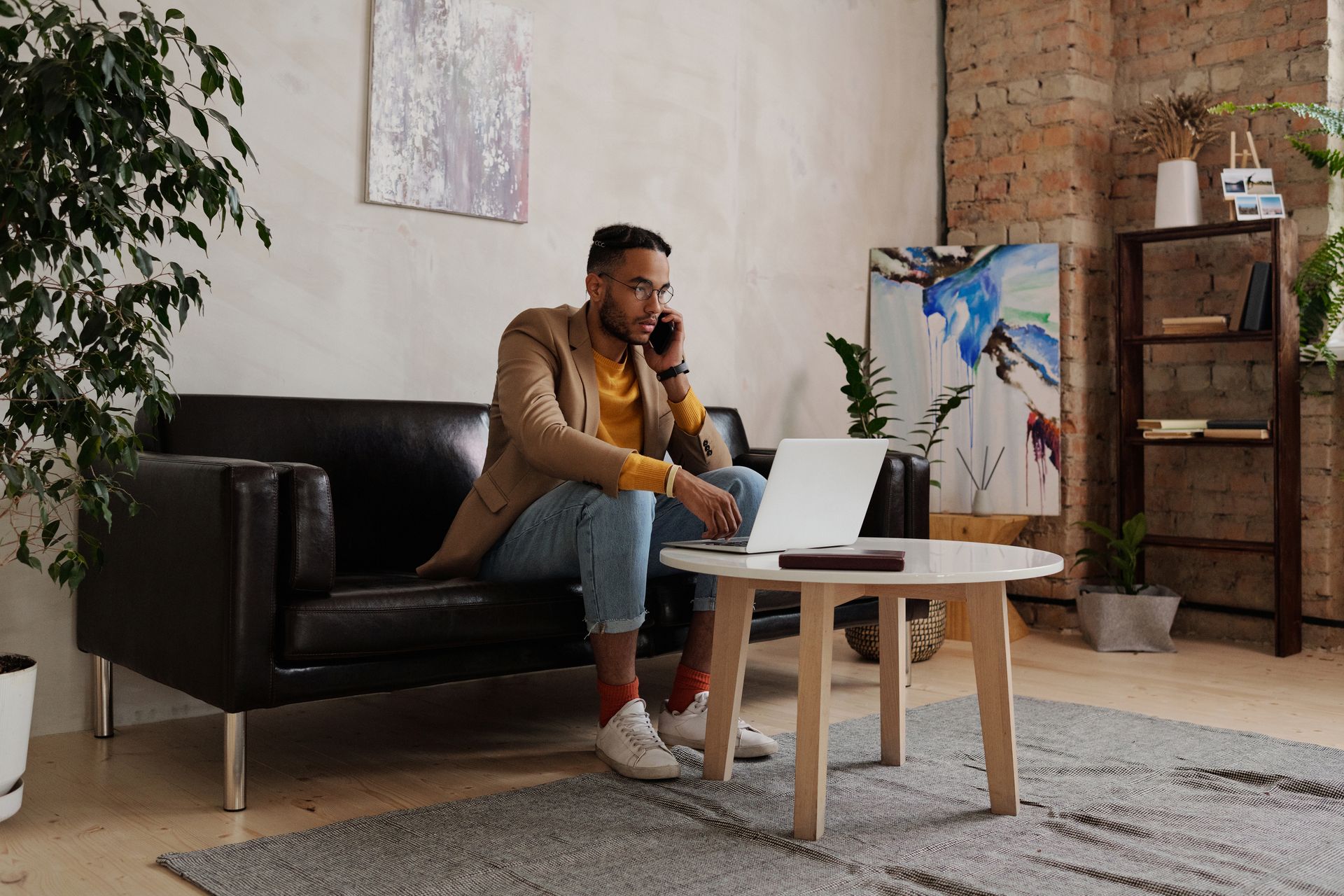 Man talking on phone while using laptop at office desk during remote work or business meeting.
